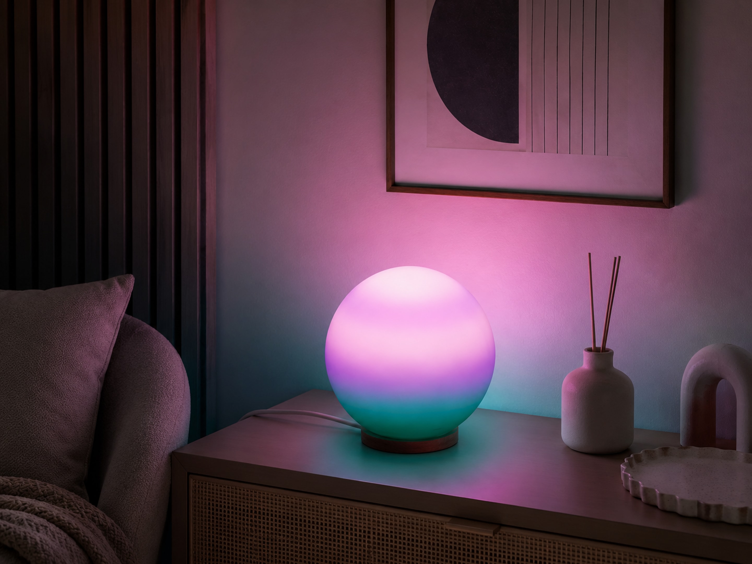 Deep table lamp glowing pink and teal on a bedroom nightstand